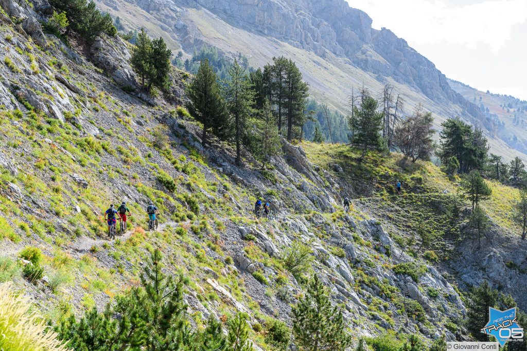 file de vététistes vus de dos sur un long sentier à flanc de montagne